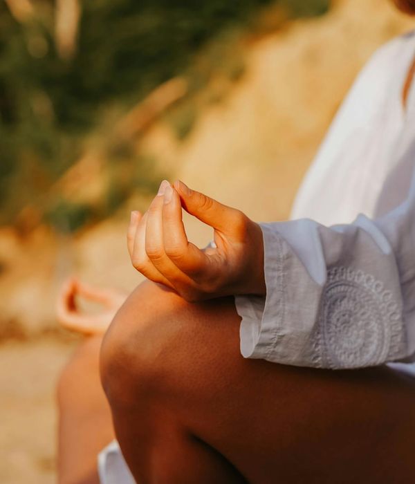 Person meditating peacefully outdoors during sunset.
